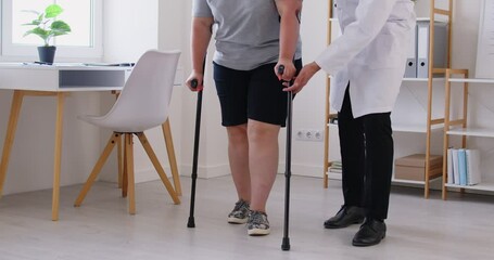 Obese woman learning to walk with crutches, during rehabilitation and physical therapy with professional nurse, manual therapy doctor, physical therapist after injuries and trauma, mobility loss