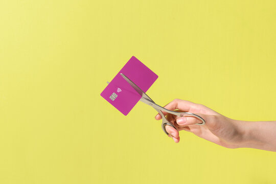 Person Cutting a Credit Card with Scissors on Yellow Background