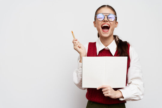 joyful student smiling with an open notebook and a pen on a plain background, showing excitement and enthusiasm for learning and studying, wearing glasses and a red sweater