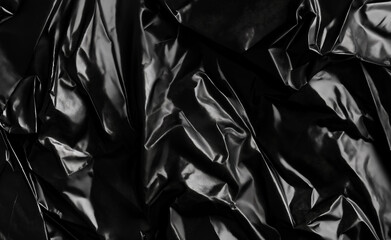 A wrinkled and glossy black plastic material forming abstract patterns and textures.