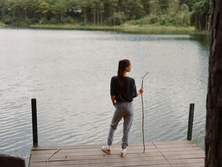Thoughtful woman standing by the lake, holding a stick, contemplating nature and solitude Peaceful...