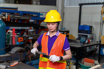 Image of Asian woman industrial engineer in vest and helmet looking and use a file to rub the surface of the workpiece for completeness in industrial workshop.