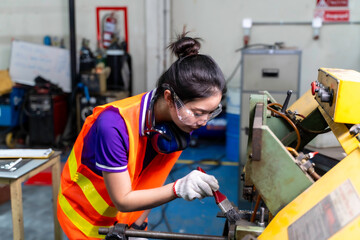 Closeup Asian woman industrial engineer in vest looking and use a cleaning brush to clean dust and scraps on the old lathe and drilling electric machine at industrial workshop.