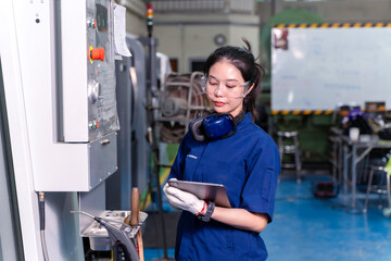 Asian woman industrial engineer wearing uniform looking and check of work on tablet with automated cnc machinery in industrial workshop.