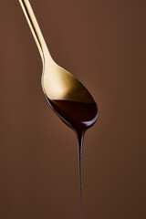 Drop of chocolate syrup hanging from the tip of a metal spoon