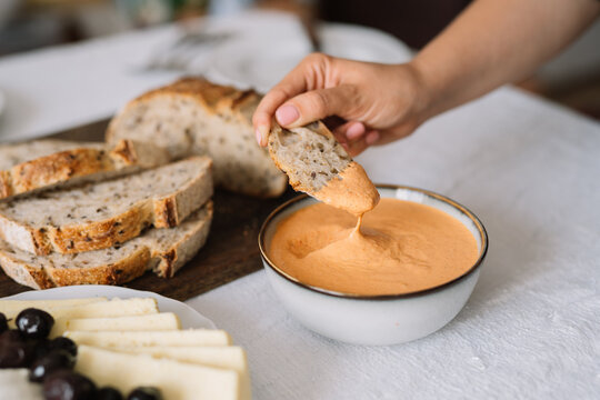 Hand dipping bread slice into creamy orange dip bowl.