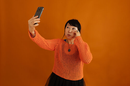 Cheerful woman puffing cheeks while taking selfie with smartphone