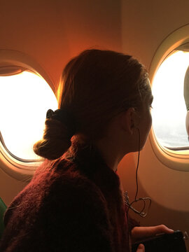 young woman looking out of airplane porthole