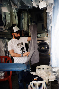 Man Ironing and Folding Laundry at Local Dry Cleaning Business