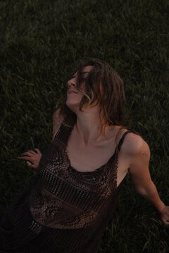 Woman lying on green grass at dusk wearing a sheer dress