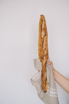 Person holding a single golden-brown baguette upright.