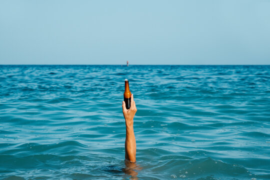 man holidng a beer bottle submerged into the ocean