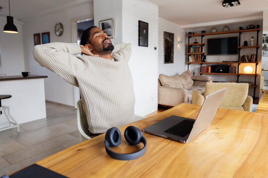 Exhausted freelancer stretching in front of laptop at table