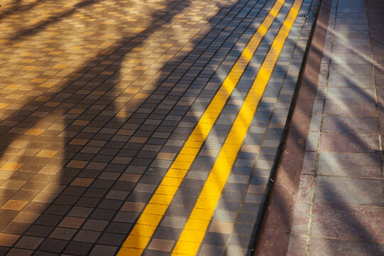 Sunlight Casting Shadows on Tiled Street with Yellow Lines