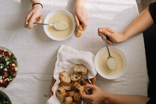 People eating soup with bread slices on a table.
