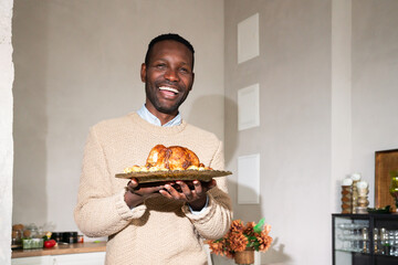 Smiling man holding oven baked chicken in the kitchen
