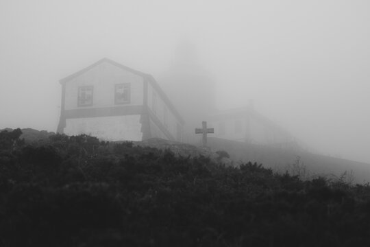 Lonely house and cross in a foggy landscape