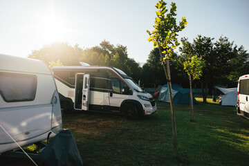 Sunny campsite with caravans, tents, and motorhomes in the morning.