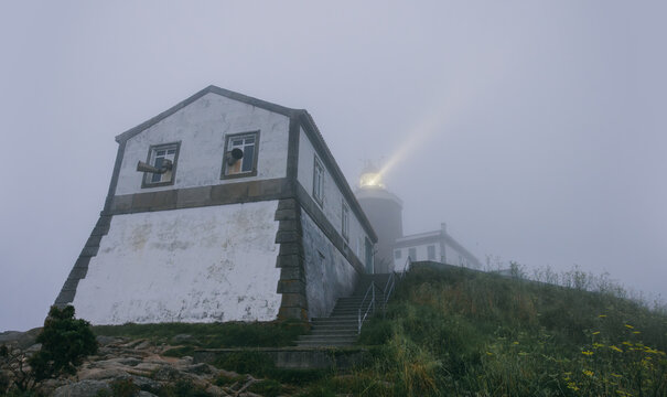 Finisterre lighthouse shining through dense fog on a rocky shore