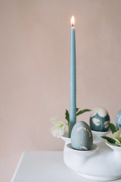 Candle with blue candle and decorated eggs in holder vase.