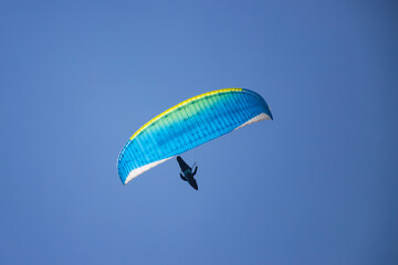 A man with a paraglider in front of a blue sky.