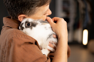 A woman hugs and holds a small decorative fluffy rabbit on her shoulder