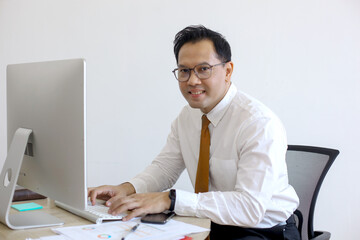 Fototapeta premium Portrait of happy businessman sitting at office desk, looking at camera and smiling.