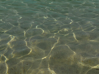 Crystal clear sea water through which you can see the bottom. Sunlight reflecting off the water.