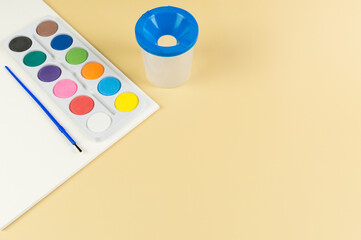 Top view of watercolor, paper, water pot and paint brush on yellow background. Painting, art, copy space, flat lay.