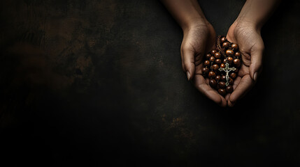 A rosary draped held in praying hands on dark background with copy space for all saints' day background banner.