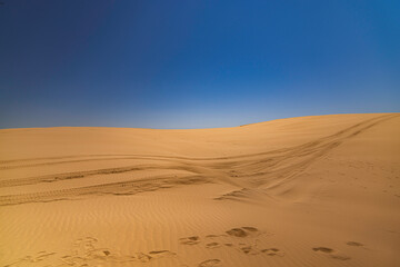 Desert sanddunes with foot tracks and blue sky