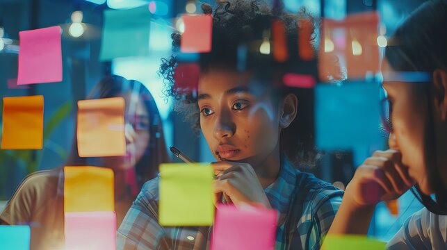 Diverse business team collaborating with sticky notes on glass office wall during strategy planning meeting