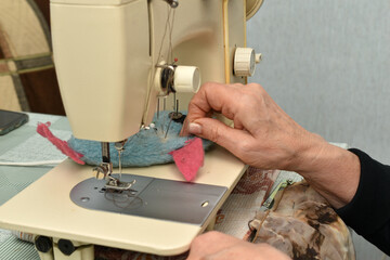 A woman's hand takes a needle from a pillow that lies on the table of a sewing machine.