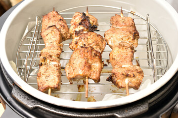 Meat on skewers is cooked in a multicooker. View from above.