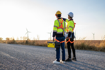 Rear view of two technicians man looking at the wind turbines field.