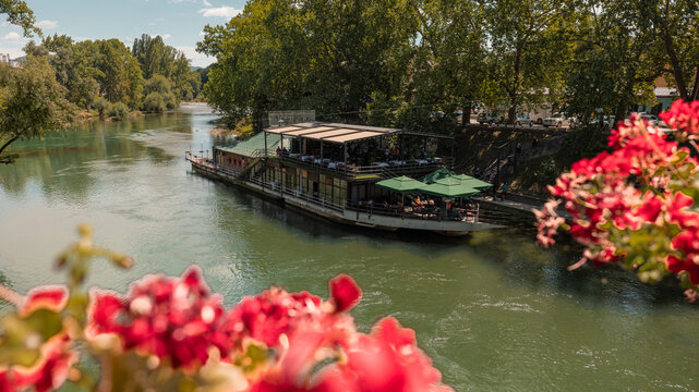 Raft or boat moored on river Vrbas in the centre of Banja Luka, used and served as a restaurant. view through some flowers from a bridge