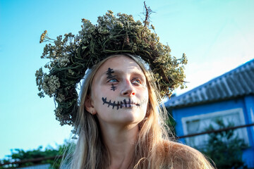 blond long-haired girl in a wreath with a painted face, Halloween, looking with a smile, national...
