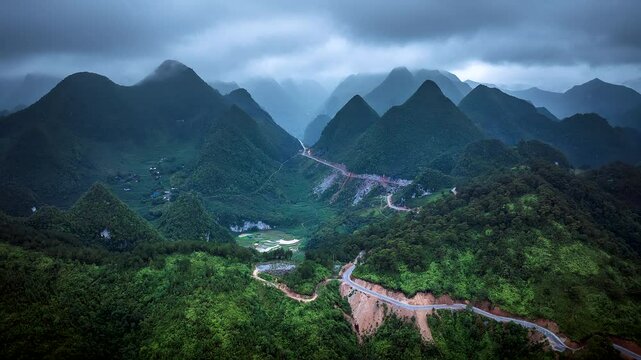 Ha Giang loop motorable road through mountain pass under rainy clouds, Natural scenery of Dong Van Karst Plateau, terraced rice fields and ethnic village, Aerial