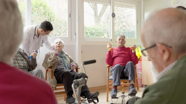 Doctor supervises an elderly man lifting small weights during a physiotherapy session in a nursing home