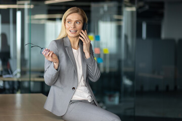 Smiling businesswoman in gray suit engaged in phone conversation in modern office environment....