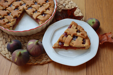 Slice of tart with dark fig jam on a white dessert plate  on wooden table with fresh figs and autumnal leaves