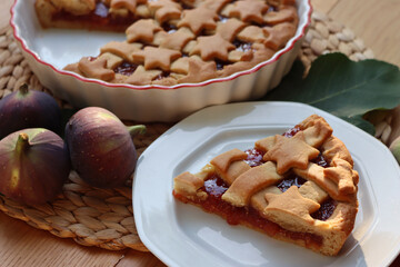 Slice of tart with dark fig jam on a white dessert plate  on wooden table with fresh figs and autumnal leaves