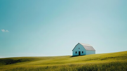 A white barn sitting on a rolling green field under a sunny, clear sky.