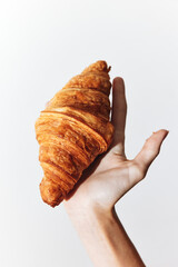Hand holding a croissant in front of a white background
