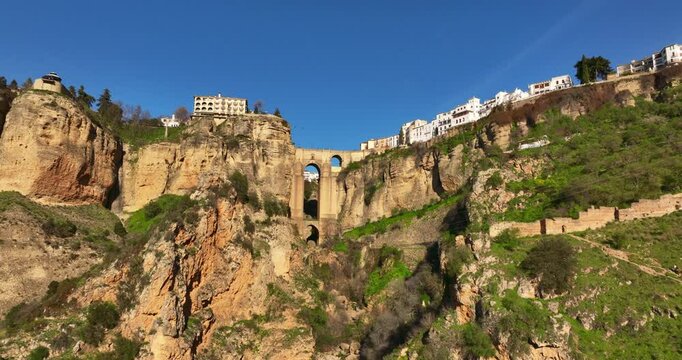 Ascending forward flying aerial shot of Ronda City in Spain, Europe. Arch bridge, homes, streets are located on the cliff. Mountains are visible in the background. High quality 4k prores footage.