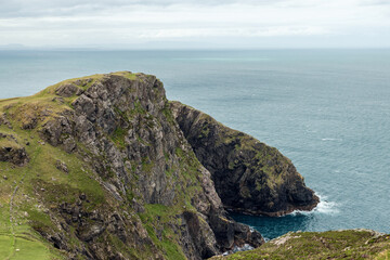 Cliffside view near Slieve League in Ireland, featuring rugged rocks, green slopes, and the Atlantic Ocean stretching to the horizon