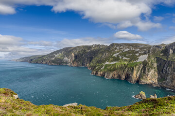 A sweeping view of the Slieve League cliffs, Ireland, with towering rock faces, vibrant green slopes, and deep blue ocean under a vast sky