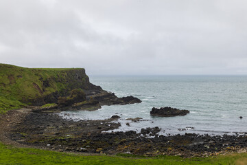 Bay of the Cow near Giant Causeway features rugged cliffs and rocky shores meeting the Atlantic Ocean under an overcast sky