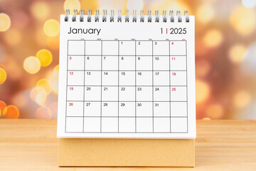 January 2025 desk calendar on wooden table with gold light bokeh.