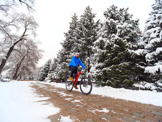 A man rides a bicycle in a winter park among snow-covered trees. Bearded cyclist in a blue jacket. Active lifestyle